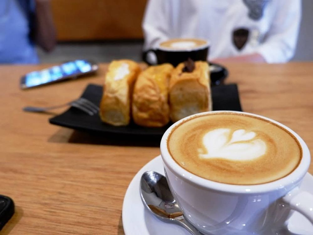 Caption: A photo of coffee in a white mug on a table with pastries in the background at Lemari Kopi, a coffee shop in South Tangerang City, Indonesia. (Local Guide Astried Marini)