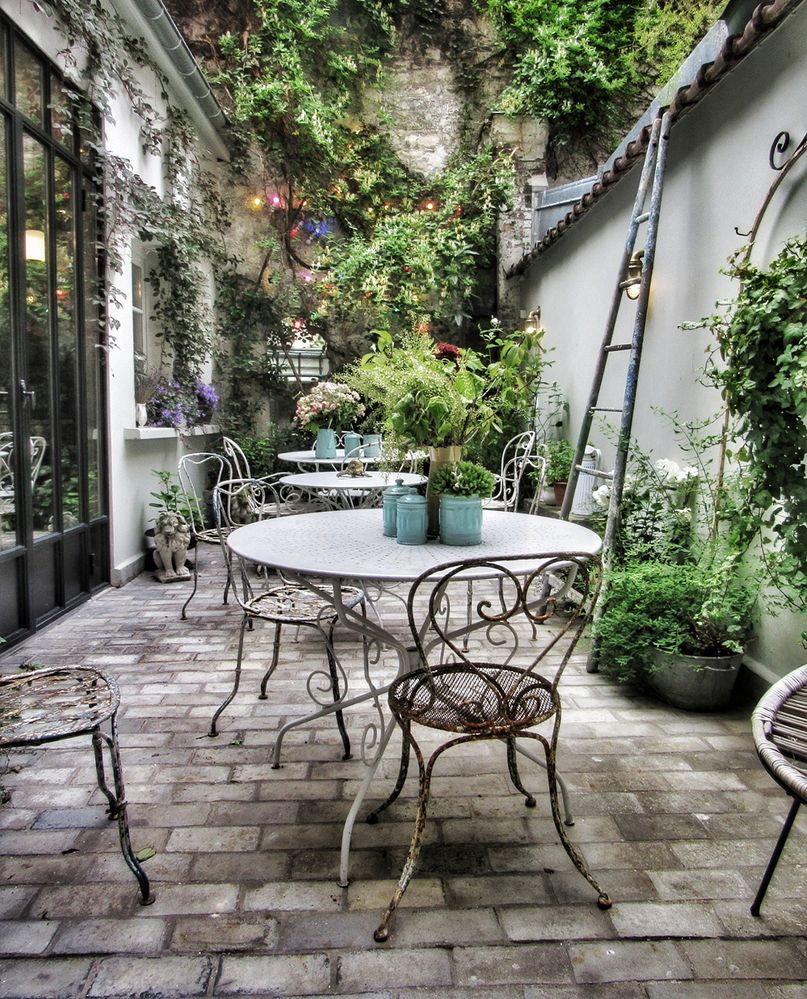 Caption: A photo of a small garden with tables and chairs at Hôtel Henriette Paris in Paris, France. (Local Guide Lindé Davies)