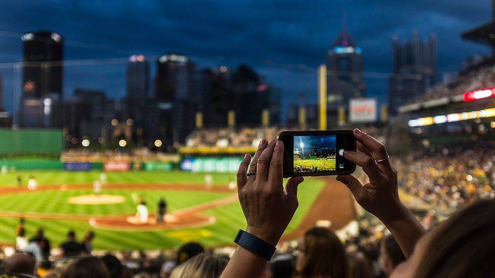 Caption: A photo of a person taking a photo of a baseball game while sitting in the stands. (Getty Images)