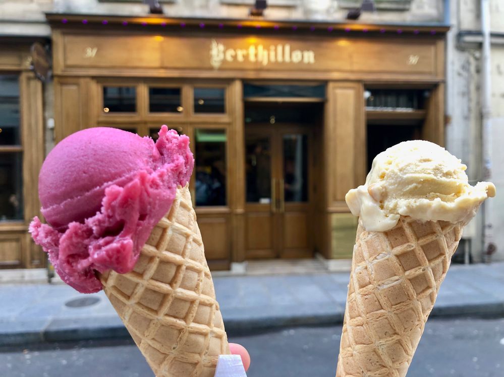 Caption: A photo of a person holding up two ice cream cones in front of Berthillon Glacier’s wood-paneled Île Saint-Louis location in Paris, France. (Local Guide Ricardo Ceu)