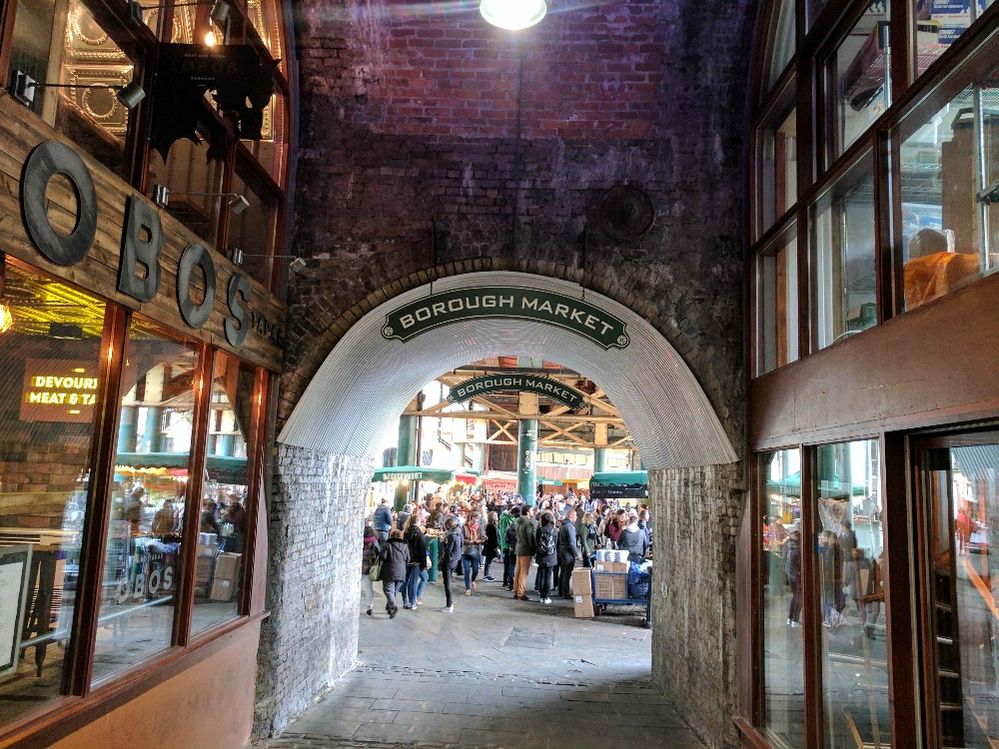 Caption: A photo of the brick arched entryway into Borough Market in London showing the large hall of vendors and shoppers in the background. (Local Guide Mercedes Findlater)