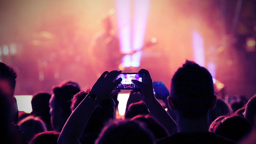 Caption: A photo of an audience member taking a photo at a concert using a smartphone. (Getty Images)