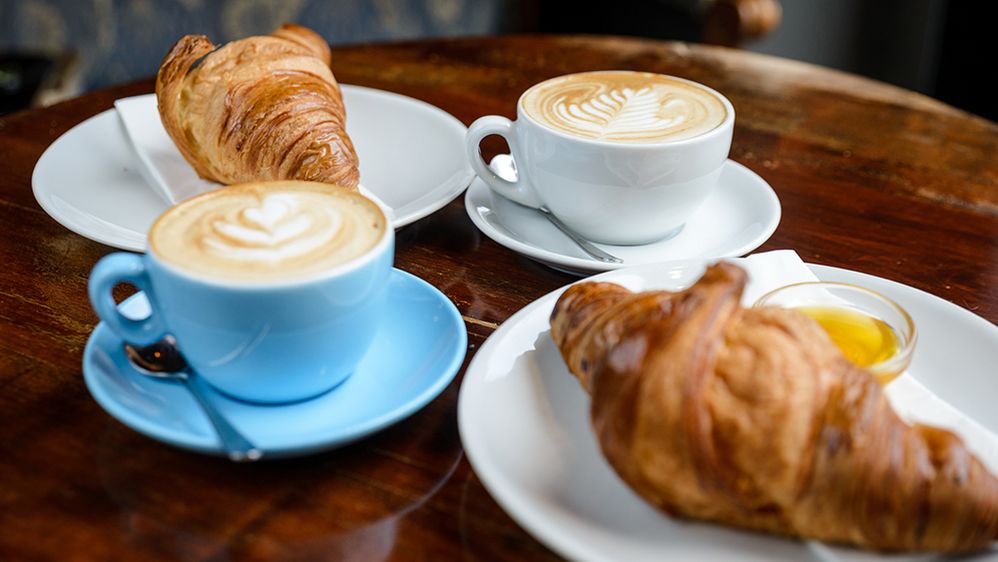 Caption: A photo of two cappuccinos and two plates of croissants on a table. (Getty Images)