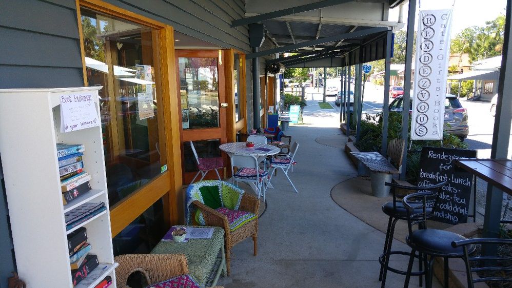 Caption: A photo of the covered patio at Rendezvous, a bookstore and cafe in Queensland, Australia, featuring tables and chairs as well as a bookshelf filled with books available for exchange.. (Local Guide Owen Davies)