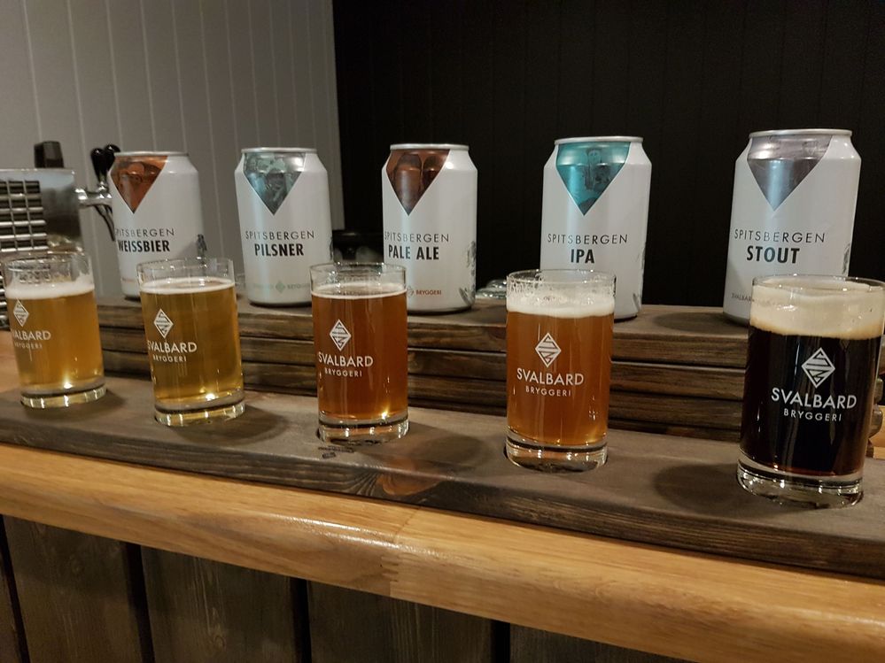 Caption: A photo of five glasses filled with different kinds of beer next to the cans they came from at Svalbard Brewery. (Local Guide Henning Furø)