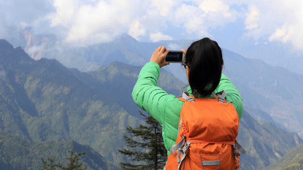 Caption: A back view of a woman backpacker taking a photo with a smartphone on a mountain peak. (Getty Images)