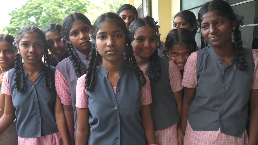 A photo of a group of girls in India wearing their school uniforms with a play button overlay over the image.