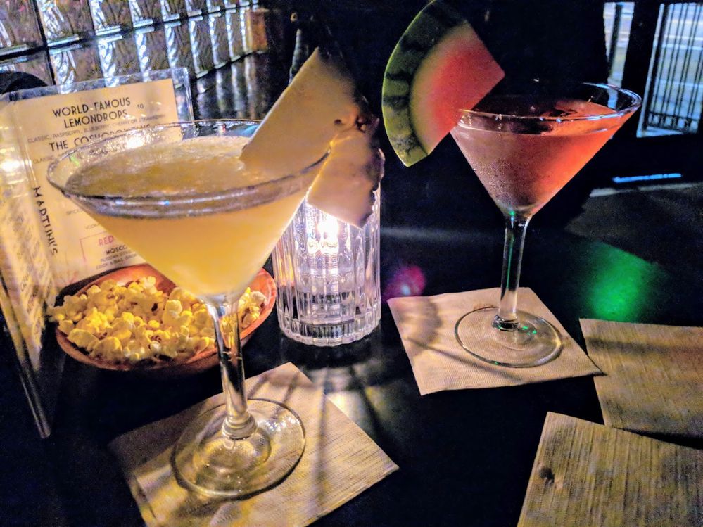 Caption: A photo of two brightly-colored martinis topped with fruit on a table next to a candle, cocktail menu, and a small bowl of popcorn. (Local Guide Corey Snidal)
