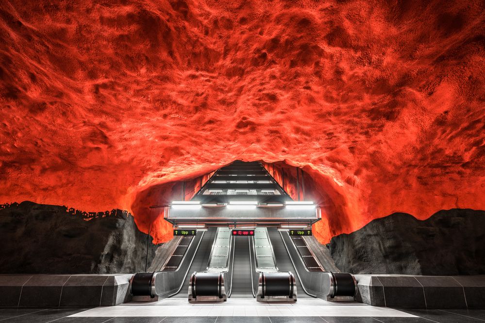 Caption: A photo of three escalators surrounded by a bright red, cave-like ceiling at Solna centrum station in Stockholm, Sweden. (Courtesy of Chris M. Forsyth)