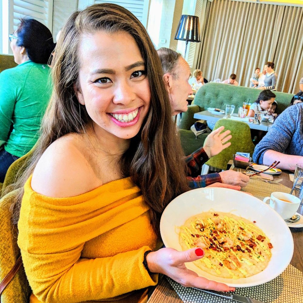 Caption: A photo of Local Guide @DDuangnet smiling while holding up a plate of cheesy grits with shrimp at Andiron Steak & Sea in Las Vegas, Nevada, United States. (Local Guide Diana Duangnet)