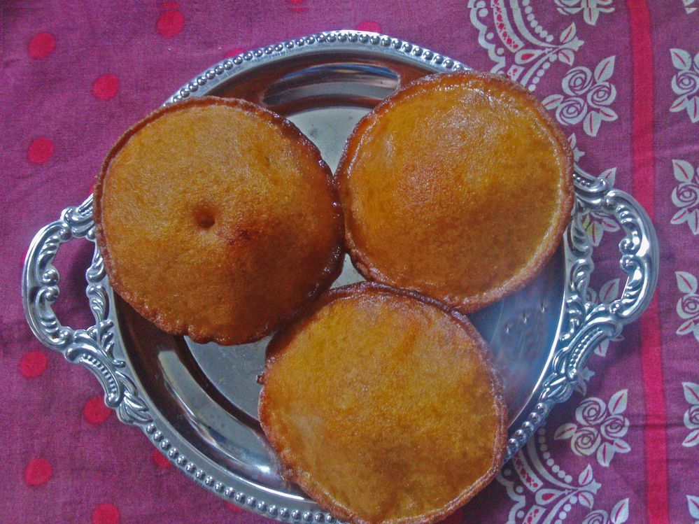 Caption: A photo of three teler pithas, a sweet, fried Bengali snack, on a silver dish on top of a pink and white table cloth. (Local Guide @MahabubMunna)