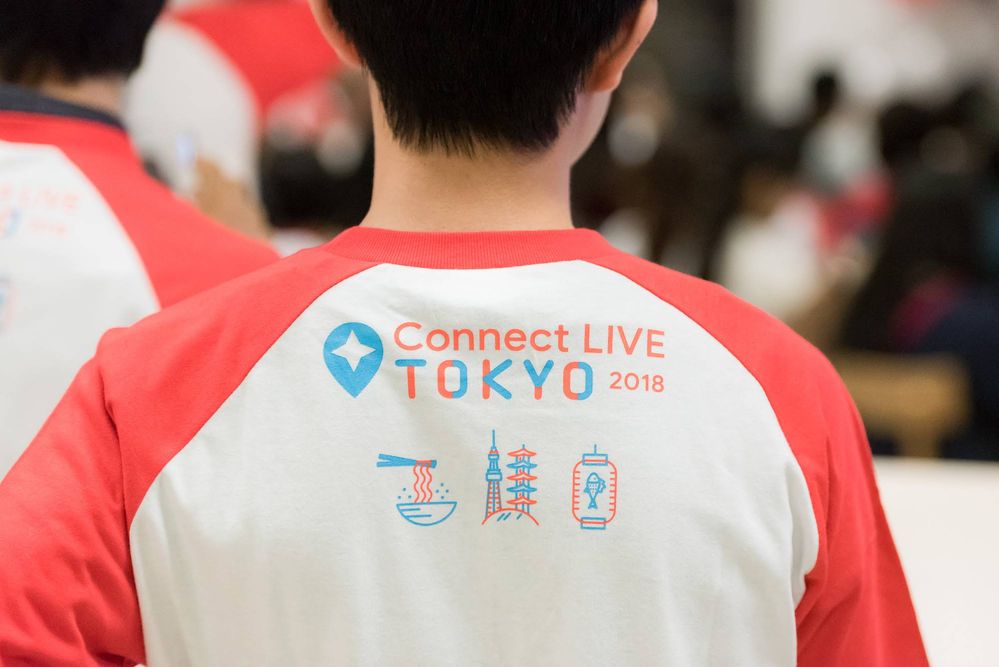Caption: A photo of the back view of a man wearing a red and white shirt that says “Connect LIVE TOKYO 2018” printed on it.