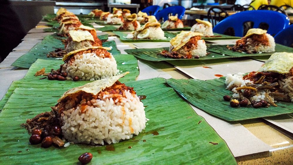 Caption: A photo of a large table filled with “nasi bungkus,” an Indonesian dish that includes rice and peanuts on top of banana leaves. (Getty Images)