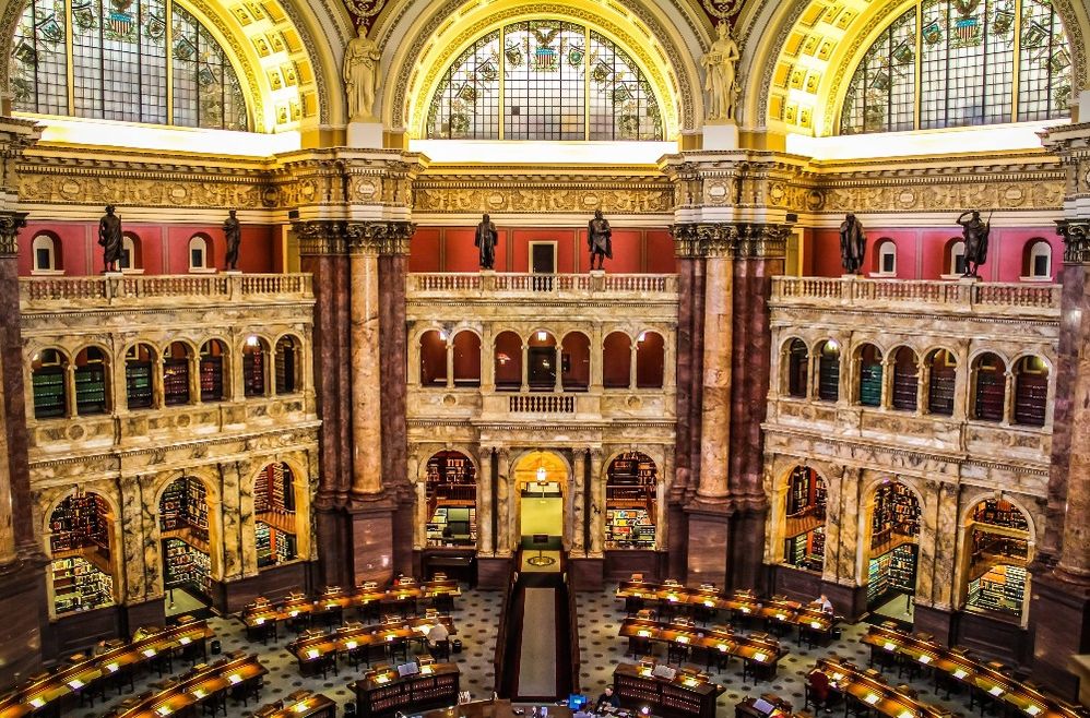 Caption: A photo of the Main Reading Room at the Library of Congress in Washington, D.C., United States. The room is filled with arches, statues, and wooden tables. (Local Guide Eddie Moy)
