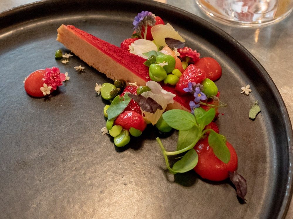 Caption: A thin slice of a cake topped with colorful fruits, vegetables, and flowers on a gray plate from Frenchie Restaurant in Paris. (Local Guide Jake Waage)
