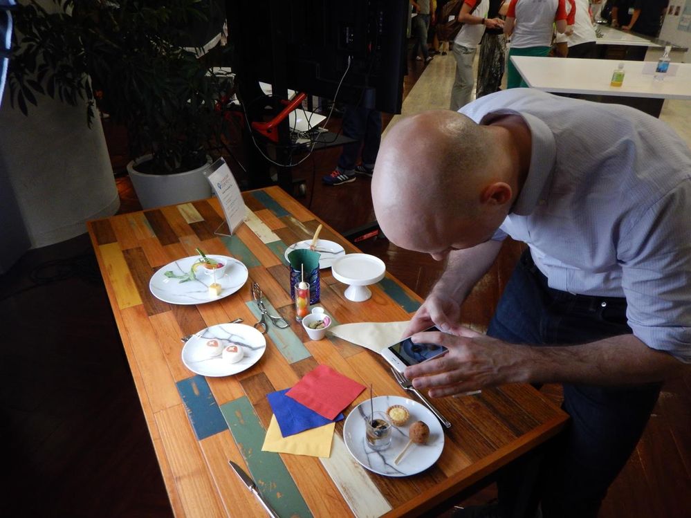 Caption: A photo of a man using a smartphone to take a photo of a plate of desserts at Connect Live Tokyo 2018.