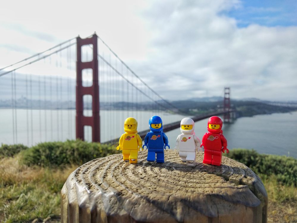 Caption: A photo of four LEGO minifigures dressed as astronauts in different colored suits---yellow, blue, white, and red, respectively---at the Golden Gate National Recreation Area on a cloudy day in San Francisco, California, USA. The Golden Gate Bridge can be seen in the background. (Local Guide Julien Ballester)