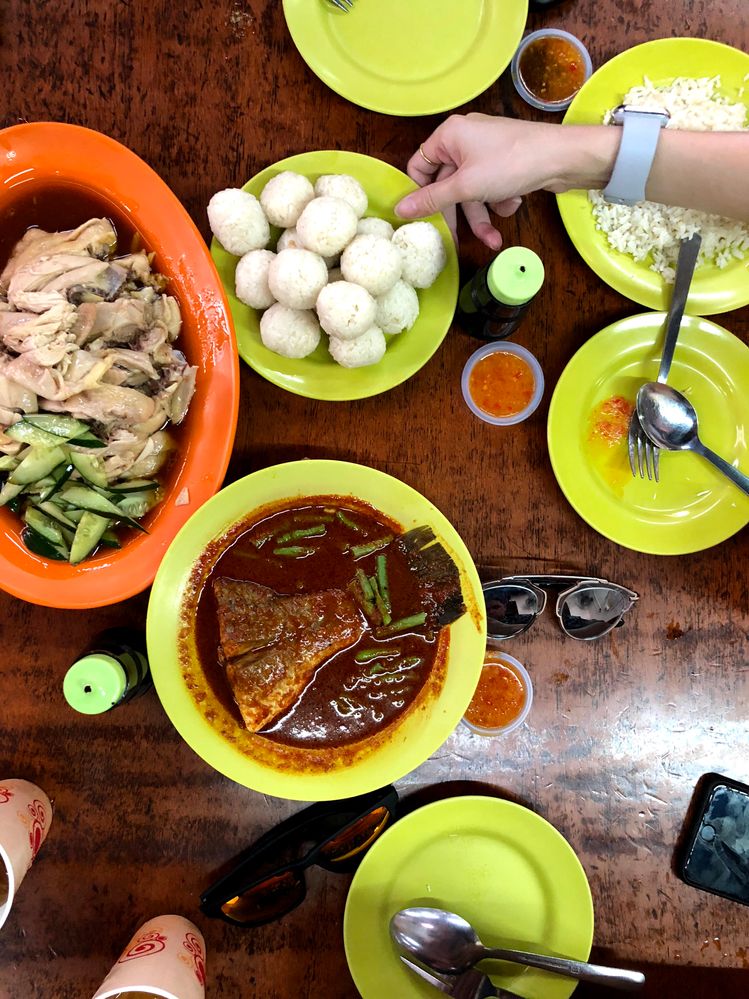 Caption: A photo of five bright green dishes and one orange dish filled with food, condiments, and utensils on a brown table at Jonker Street Market in Malacca, Malaysia. (Local Guide Eddie Stewart)
