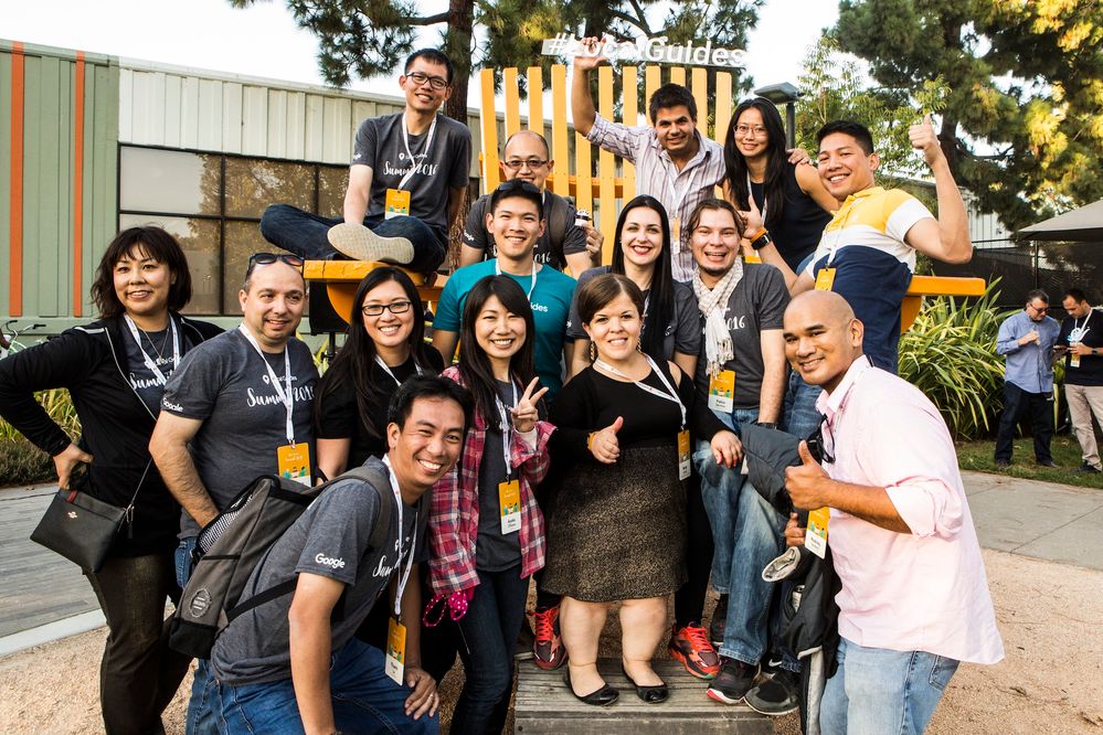 Caption: A photo of a group of Local Guides on a giant chair smiling and gesturing at the camera during the Local Guides Summit in 2016.