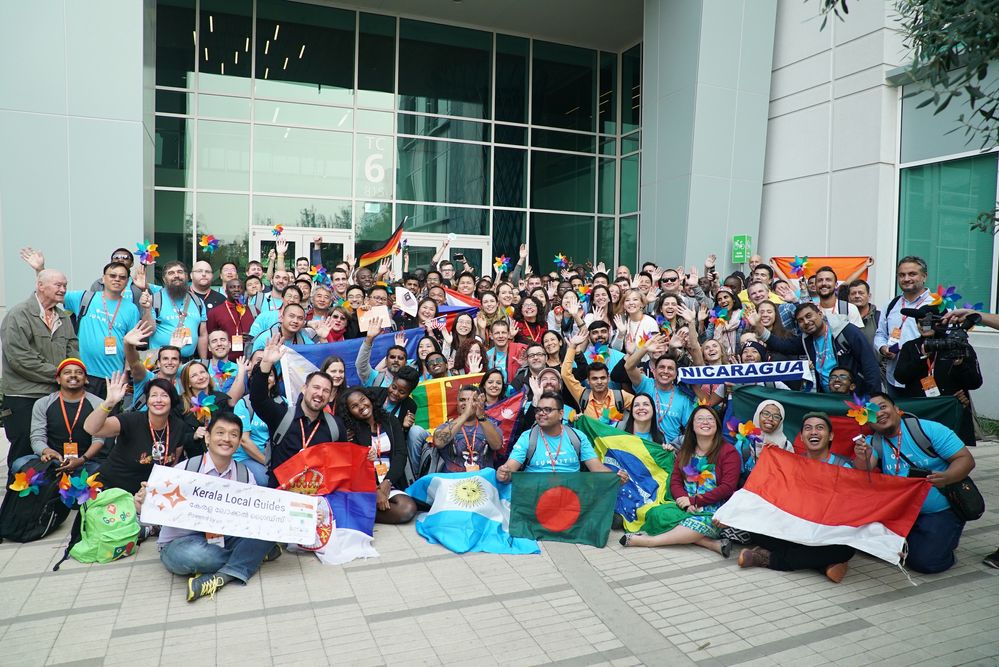 Caption: A group photo of the Local Guides Summit 2017 attendees holding up flags and signs from their home countries.