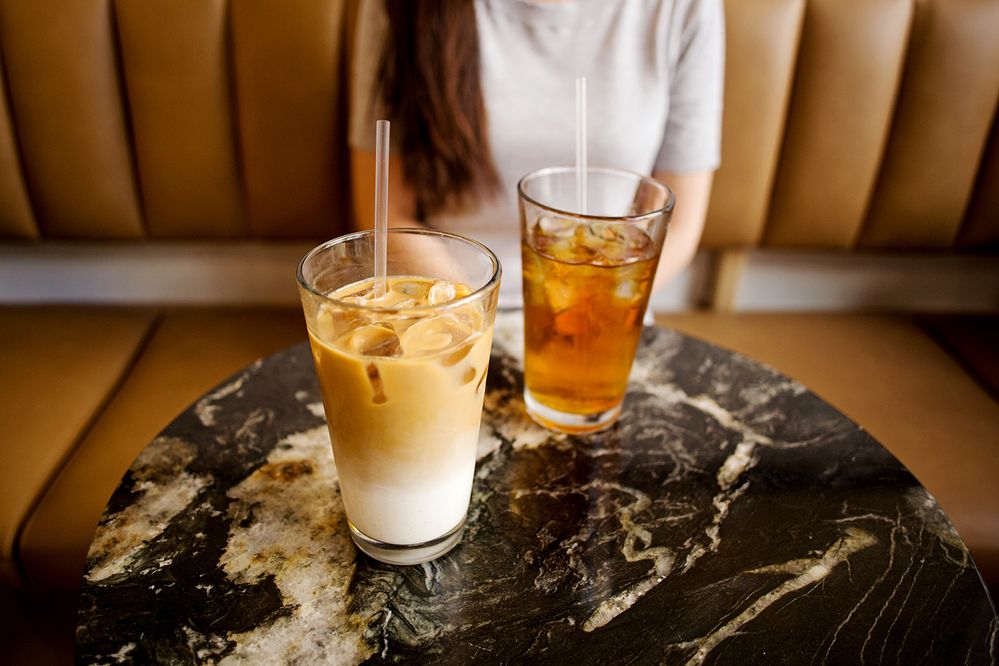 Caption: A photo of an iced coffee and another iced beverage with clear plastic straws on a marble table at Café Humble Lion in Montreal, Canada. (Local Guide Lena Han)