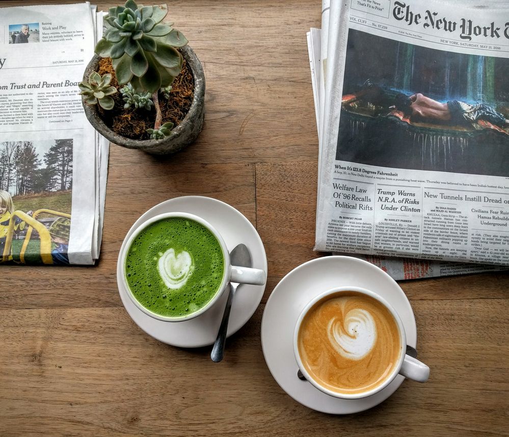 Caption: A photo of a coffee drink and a matcha drink in white cups on a table next to a potted plant and newspapers. (Local Guide Remi Hashimoto)