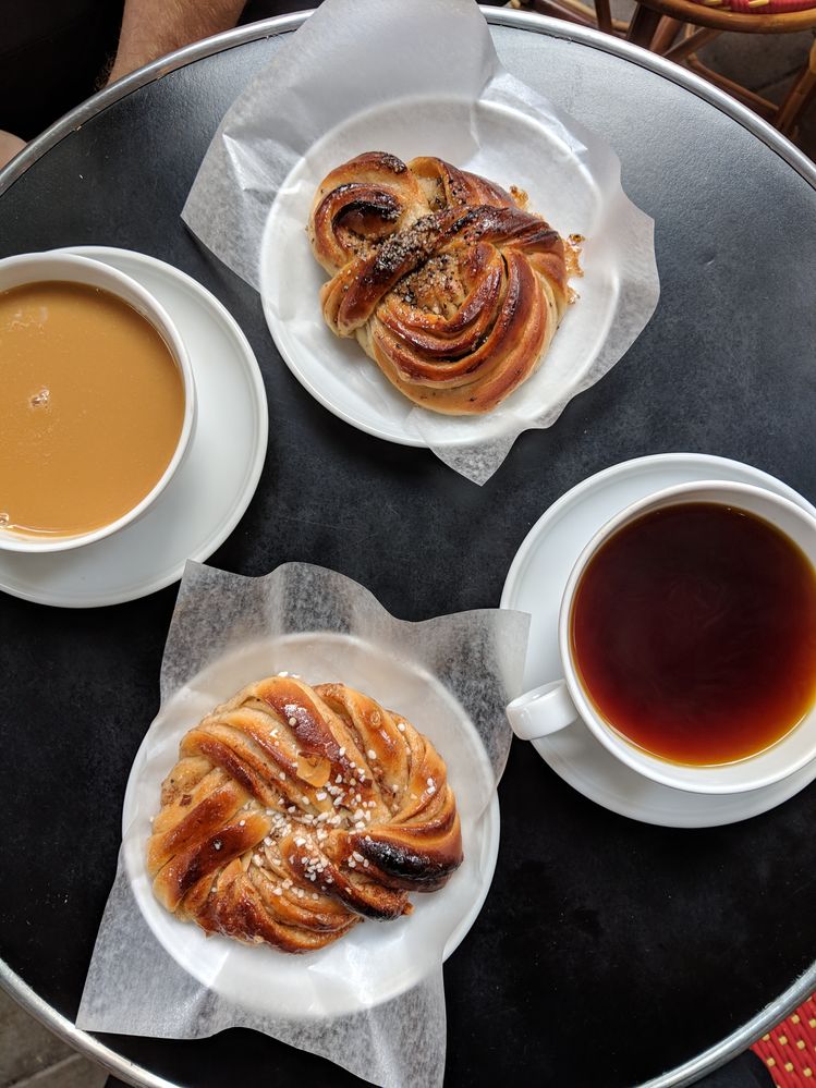 Caption: A photo of two Swedish cinnamon rolls on plates next to two oversized cups of coffee on a round bistro table at Bageri Petrus in Stockholm, Sweden. (Local Guide Nina Fitton)