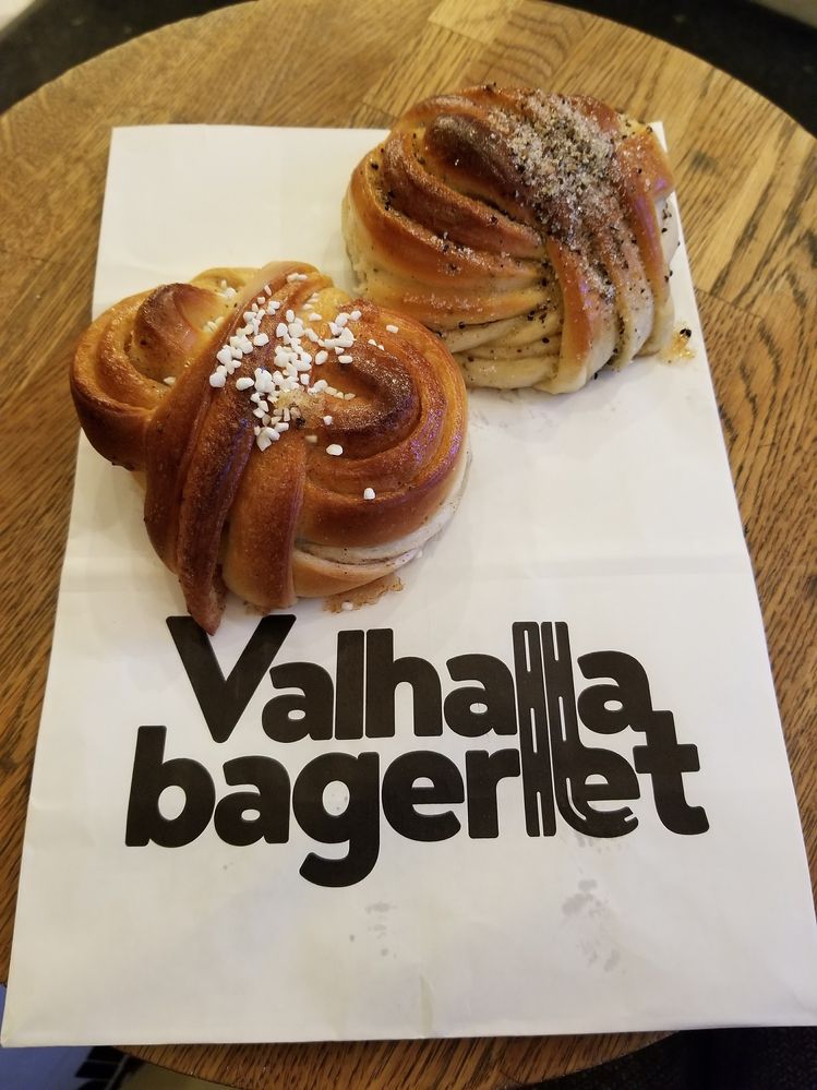 Caption: A photo of a Swedish cinnamon roll with sugar crystals on top and a cardamom bun on top of a white paper bag printed with “Valhallabageriet,” a bakery in Stockholm, Sweden. (Local Guide Megan E)