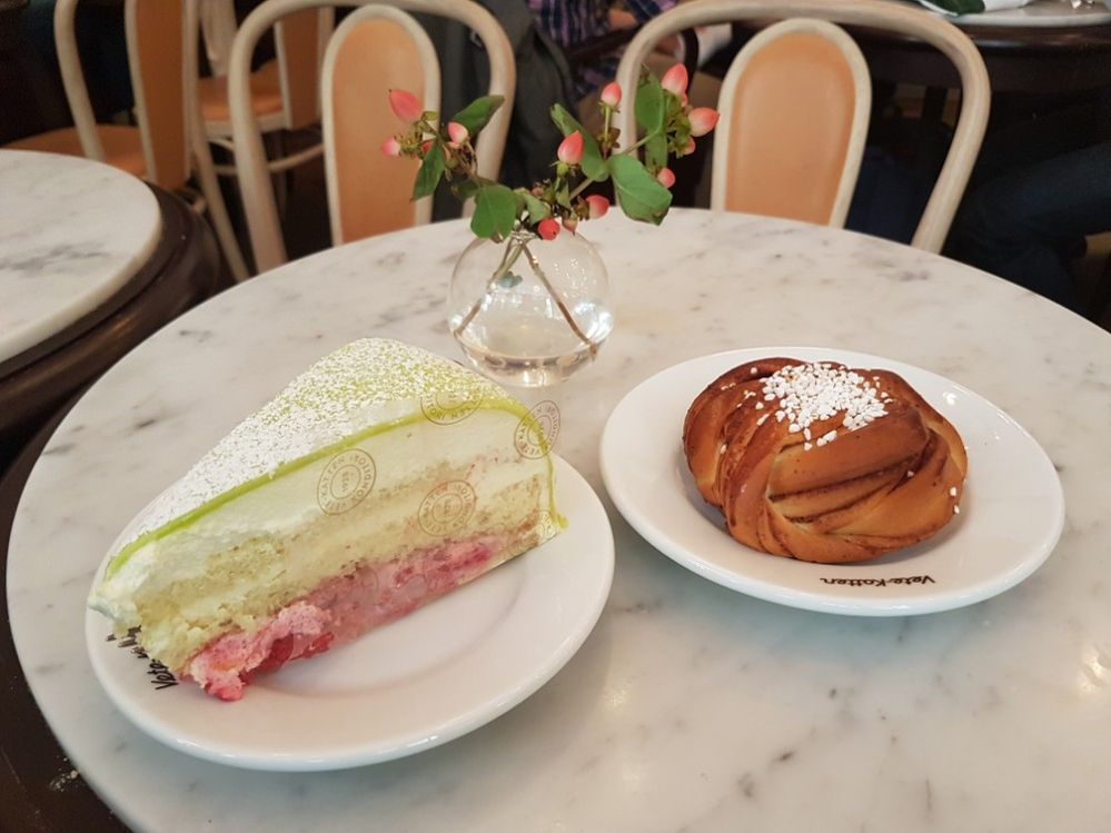 Caption: A photo of a Swedish cinnamon roll and princess cake with green icing on a marble tower with a small flower in a vase at Vette-Katten in Stockholm, Sweden. (Local Guide Carlos Villa Blanco)