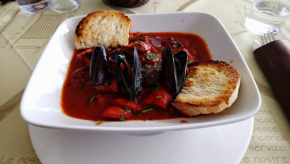 Caption: A photo of cacciucco, a fish stew popular in northwest regions of Italy, in a white bowl with two toasted pieces of bread. (Local Guide @adrianaS2)