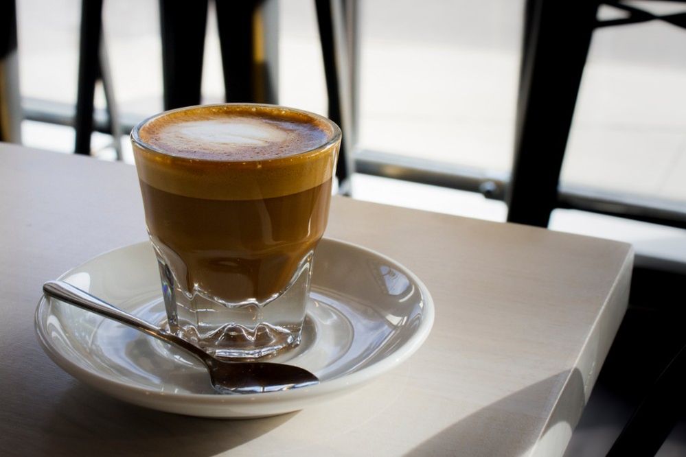 Caption: A photo of a cortado in a glass cup on a white saucer next to a small spoon at Blonde Biscotti in Houston, Texas, USA. (Local Guide Daniel Ngo)