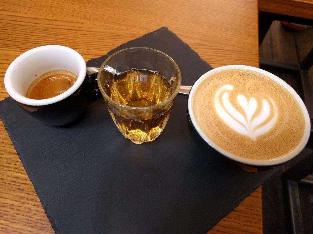 Caption: A photo of London coffee shop Kaffeine’s coffee tasting flight, which includes a shot of espresso, a single-shot cappuccino, and cascara, on a black napkin on a table. (Local Guide John Hawkins)