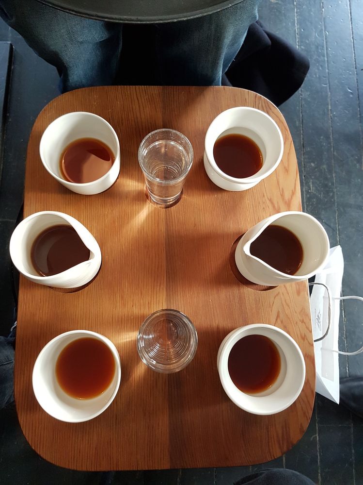 Caption: A photo of four white mugs, two small white pitchers with coffee in them, and two glasses of water on a wooden board, which make up the Aeropress coffee flight at Tim Wendelboe coffee shop in Oslo, Norway. (Local Guide Scott Martin)