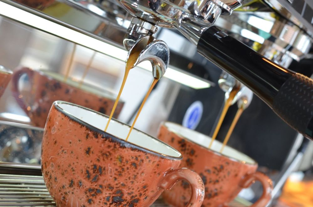Caption: A photo of a coffee machine pouring coffee into two orange and black mugs at Harris + Hoole in Hornchurch, UK. (Local Guide James Morgenstern)