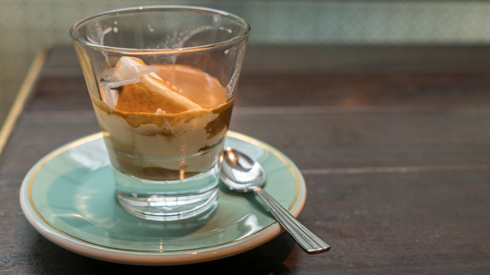 Caption: A photo of affogato, an Italian coffee drink, in a glass cup on a small light blue plate next to a silver spoon. (Getty Images)