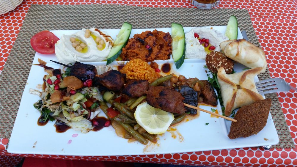 Caption: A photo of a rectangular plate piled with vegetarian food including hummus, vegetables, and more on a red-and-white tablecloth at Haus Hitl in Zurich. (Local Guide Russell Horton)