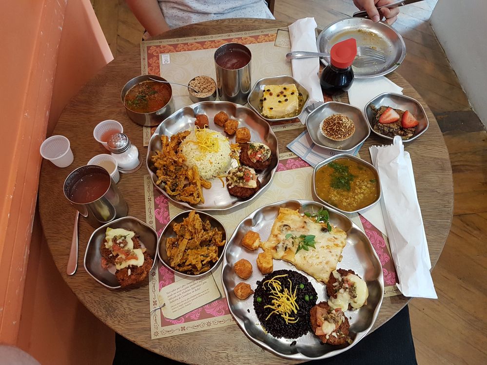 Caption: A photo of many large and small circular stainless steel dishes filled with different types of food on a wooden table at Gulab Hari restaurant in São Paulo. (Local Guide Renan Uzum)