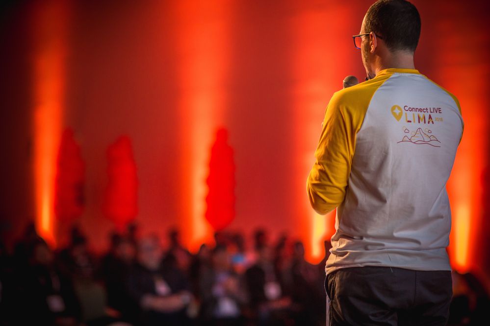Caption: A photo of the back of Local Guides Program Manager, @JuanCh, wearing a Connect Live Lima T-shirt while speaking on stage at Connect Live Lima 2018.