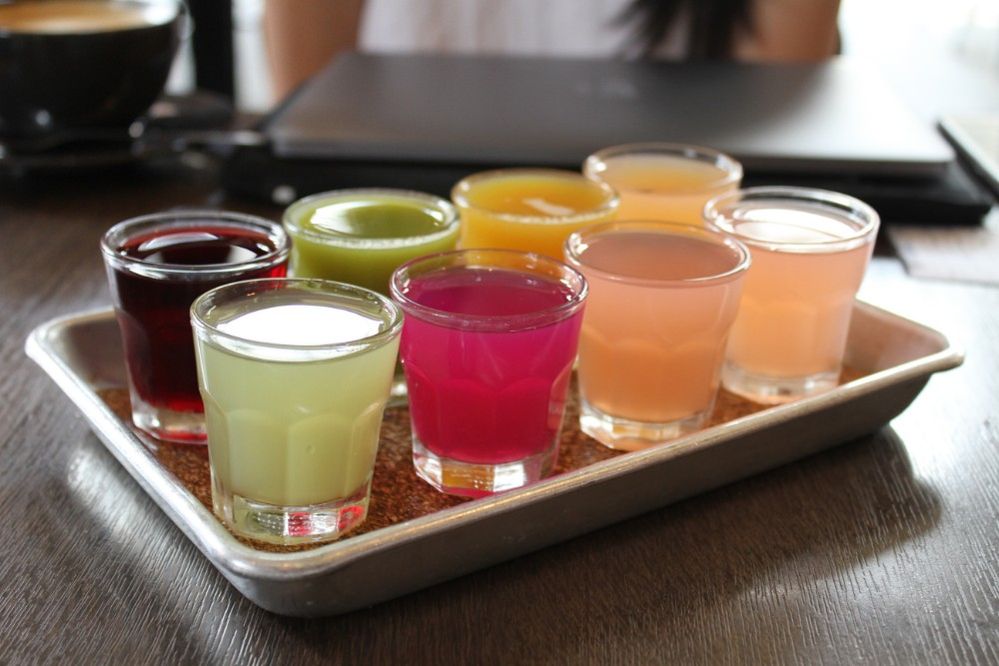 Caption: A photo of eight different small cups of colorful juices on a metal train at Tout Suite in Houston, Texas, USA. (Local Guide Daniel Ngo)