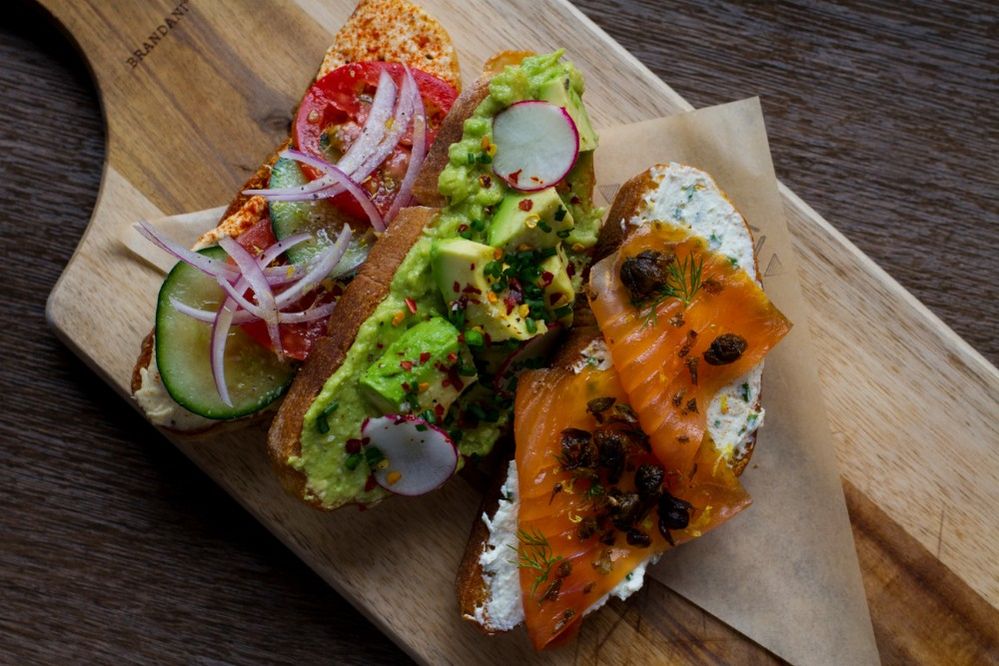 Caption: A photo of three different kinds of toasts on a wooden board. One with tomato, cucumber and red onion (left), one with avocado, radish, and spices (middle), and one with cheese and smoked salmon (right). (Local Guide Daniel Ngo)