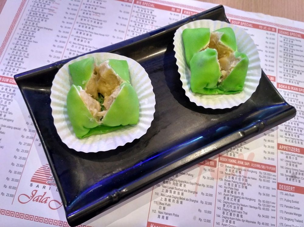 Caption: A photo of two durian pancakes on white baking cups on a black rectangular plate on top of a menu at Sari Laut Jala Jala Kuningan City in Jakarta, Indonesia. (Local Guide Febrina Paramita)