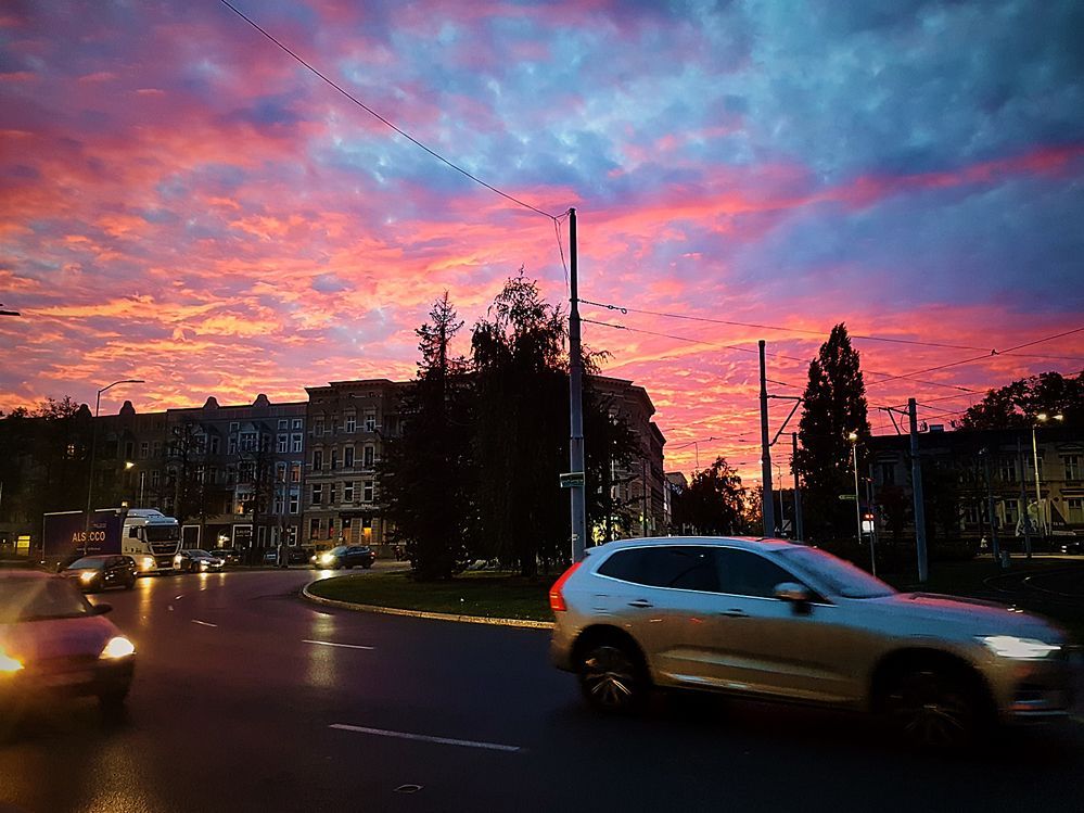 Caption: A photo of the sunset with pink, purple, blue, and yellow clouds in the sky above a street with cars in Szczecin, Poland. (Local Guide @SergV)