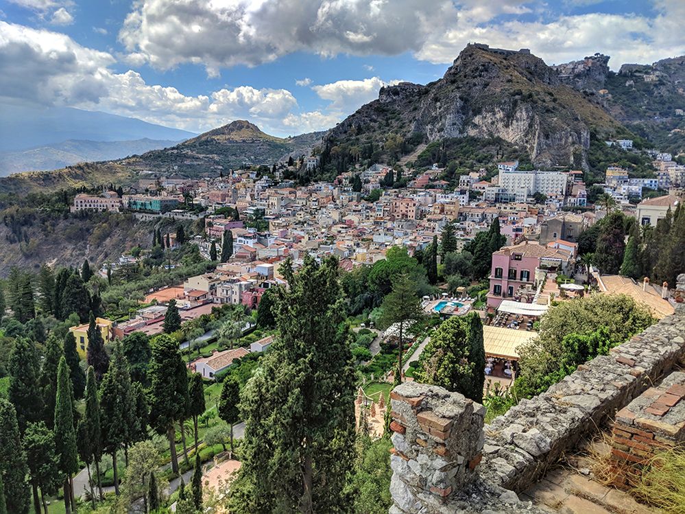Caption: A bird’s-eye view photo of houses, buildings, trees, and mountains in the city of Taormina, Italy taken on a partly cloudy day. (Local Guide Adrian Lunsong)