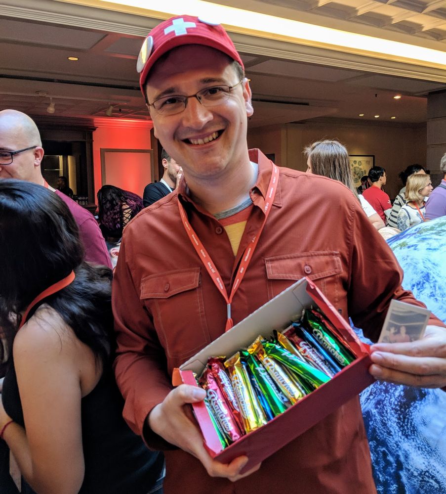 Caption: A photo of Local Guide Michael holding up a small polaroid and a box of Swiss chocolates packaged in different colored wrappings at Connect Live 2018.