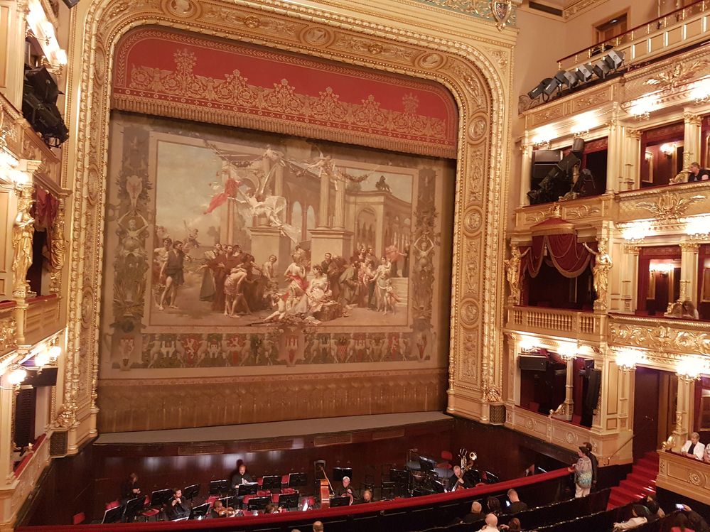 Caption: A photo of the red and gold, multi-level interior of the National Theatre in Prague, Czechia, showing the stage and painted curtain. (Local Guide Konstantin Porotchkin)