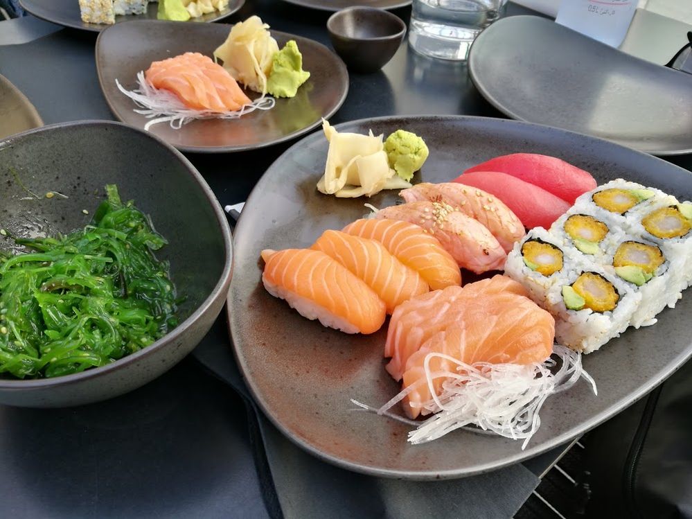 Caption: A photo of a plate of sushi next to a bowl of seaweed salad and other plates of food on a table at Sushi Art, Dubai, UAE. (Local Guide Benny J.)