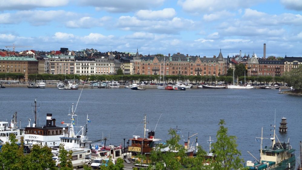 Caption: A photo of Stockholm taken from the Moderna Museet modern art museum looking out onto colorful boats in Stockholm Harbor and views of brick buildings in the Östermalm neighborhood. (Local Guide philippe salgarolo)