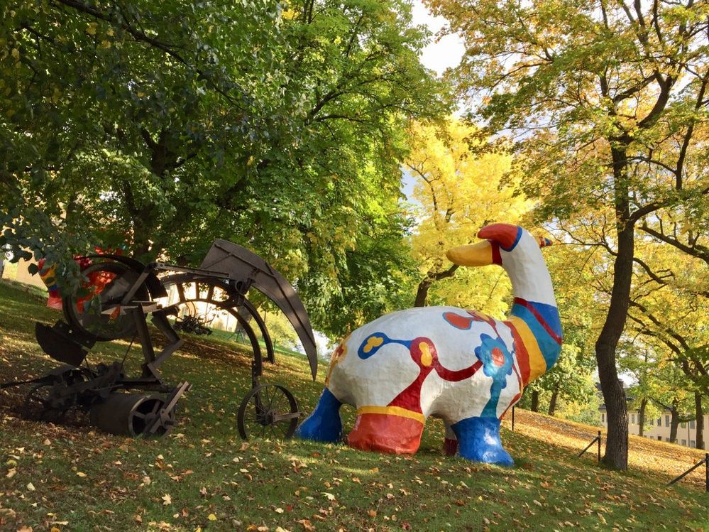 Caption: A photo of two sculptures outside of Stockholm’s Moderna Museet, one made of metal with a steampunk look, and the other a colorful sculpture by Niki de Saint Phalle. (Local Guide Shan Cheng)