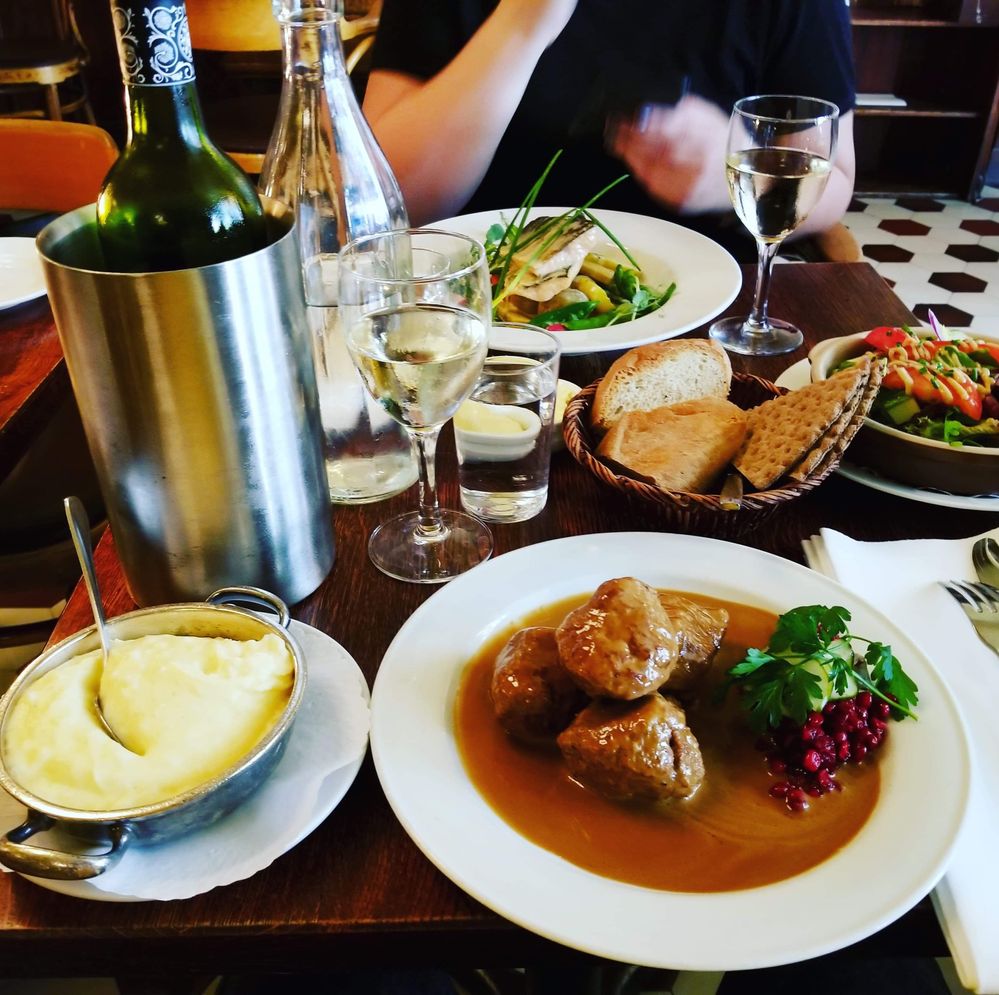 Caption: A photo of the Swedish meatballs from Restaurant Pelikan in Stockholm, showing the meatballs in gravy on a white plate with lingonberries, a side of mashed potatoes, a fish dish, and a bottle of white wine along with two glasses. (Local Guide Christina Deveau)