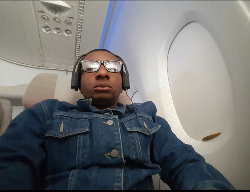 Caption: Photograph showing a Local Guide in an airplane wearing blue denim  jacket, glasses and headphone
